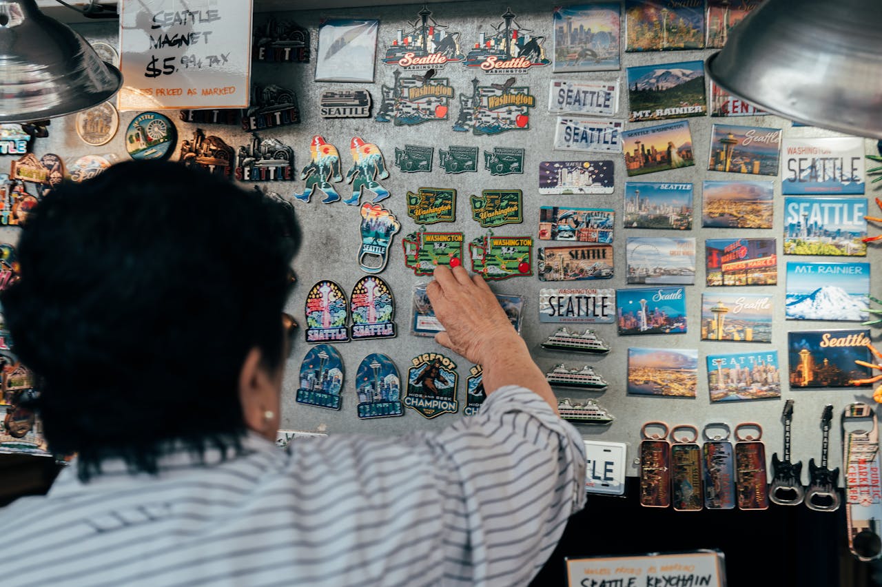 about-01 A person browsing a variety of Seattle-themed souvenir magnets at a market.